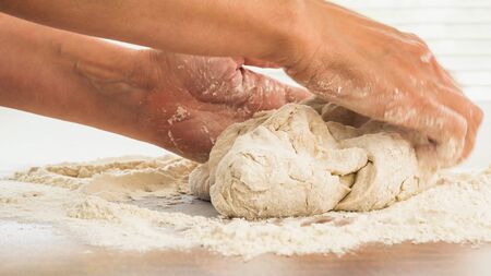 Bread dough or pizza dough close up on wooden kitchen table. Woman hands kneading whole wheat flour bread doughの写真素材