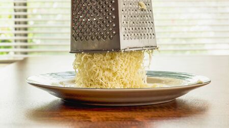 Grated Mozzarella Cheese and grater close up on a wooden kitchen tableの写真素材