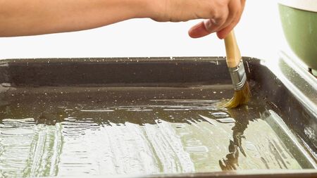 Greasing baking sheet with olive oil. Woman hands, close up on white backgroundの写真素材