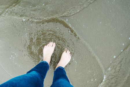 Woman legs in blue jeans standing in the sea water, view from aboveの写真素材