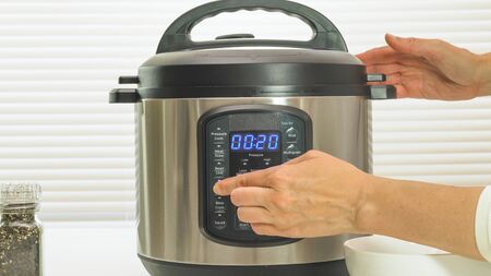 Multi cooker close up on kitchen table. Woman pushing button, the timer counts up.の写真素材