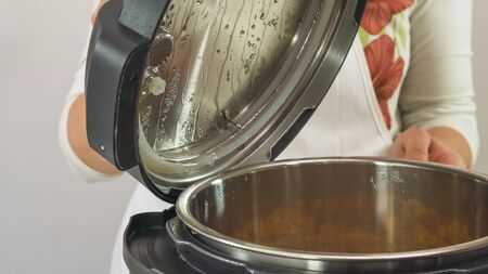 Woman lifting multi cooker lid. Cooking soup in modern electric multi cookerの写真素材