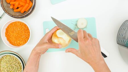 Lentil soup recipe. Chef peeling white onion, close up view from above, white kitchen table backgroundの写真素材
