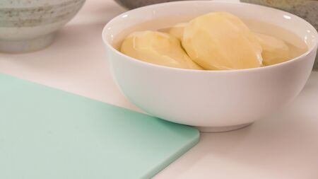 Peeled potato in a bowl close up on white kitchen tableの写真素材