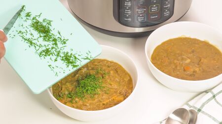 Creamy lentil soup close up on kitchen table. Cook adds fresh dill in a bowl