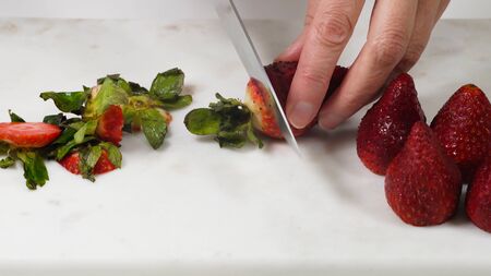 Woman cutting fresh ripe strawberries for dessert, close up on white backgroundの写真素材