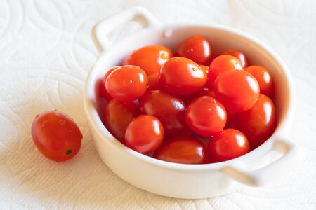 Cherry tomatoes in a small glass bowl close up on white backgroundの写真素材