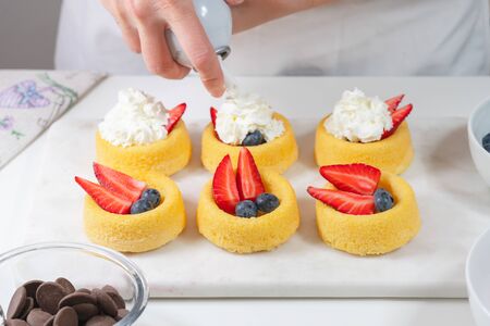 Biscuit cakes with fresh berries, chocolate, and whipped heavy cream. Fresh mini biscuit cups close up on white background, woman handsの写真素材