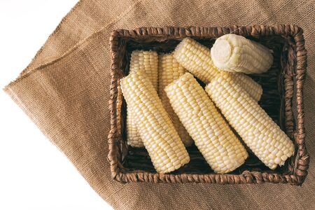 Corn in a basket. Raw organic corn in wicker basket close up isolated on white backgroundの写真素材