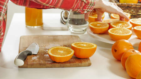 Woman cuts oranges on a wooden kitchen board with white background. Preparing fresh orange juice using an electric juicer.の写真素材