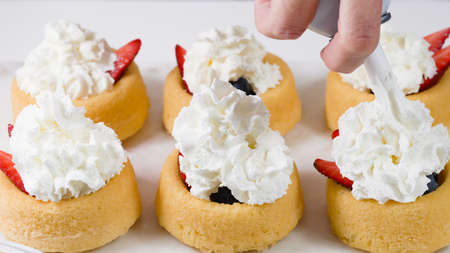 Biscuit cakes with fresh berries, chocolate, and whipped heavy cream. Woman preparing dessert, mini biscuit cups with strawberries and blueberries,  close up on white backgroundの写真素材
