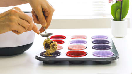 Bran muffins with dry cranberries recipe. Filling silicone cups with muffin batter close up on white backgroundの写真素材