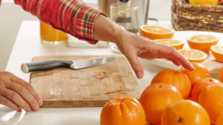 Woman cuts oranges on a wooden kitchen board with white background. Preparing fresh orange juice using an electric juicer.の写真素材