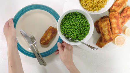 Golden batter deep fried fish fillet, served with green peas, sweet corn, and slices of lemon close up on a plate on white backgroundの写真素材