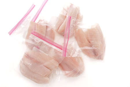 Tilapia fish fillet in plastic zip lock bags close up on white background, directly from aboveの写真素材