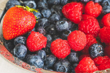 Fresh ripe washed strawberries, blueberries, raspberries in colander close up on white backgroundの写真素材