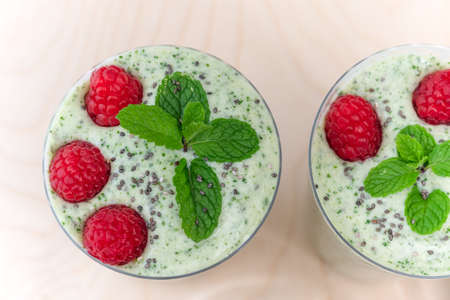 Celery banana smoothie with mint and fresh raspberries in glasses close up on wooden background, view from aboveの写真素材
