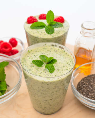 Celery spinach banana smoothie with Chia seeds, honey, fresh raspberries and mint leaves close up on wooden serving board on white backgroundの写真素材