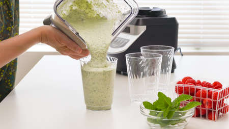 Celery banana smoothie with Chia seeds and honey in glasses, served with fresh raspberries and mint leaves, close up on kitchen table. Healthy breakfast, dessert, green detox smoothie recipeの写真素材