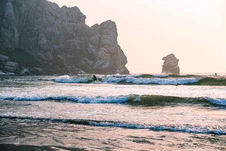 Morro Bay State Park, California/USA  - September 13, 2020.  Surfing at Marro Bay at sunset, California Coastline. Stormy ocean, and famous Marro Rock at sunsetのeditorial素材