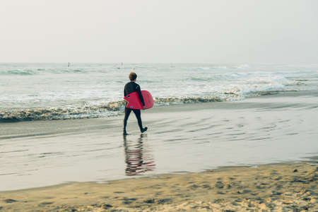 Morro Bay State Park, California/USA  - September 13, 2020.  Surfer with surf board walking on the beach. Morro Bay, Californiaのeditorial素材
