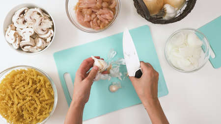 Pasta with chicken and mushrooms recipe. Raw ingredients close up on kitchen table. Chef peeling garlicの写真素材