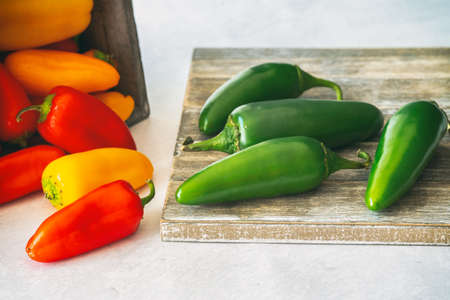 Jalapeno peppers close up on wooden cutting board and wooden box of red and yellow bell peppersの写真素材