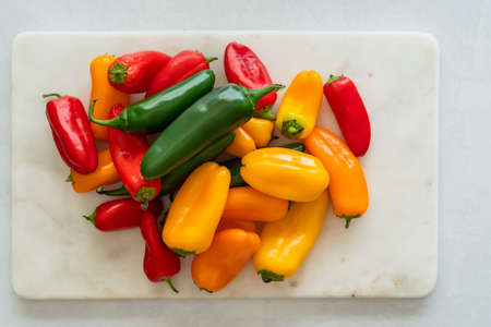 Fresh peppers assortment. Red pepper, yellow pepper, and jalapeno peppers close up on marble cutting board directly from aboveの写真素材