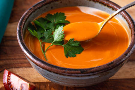 Creamy tomato soup with fresh parsley close up in a bowl on wooden background