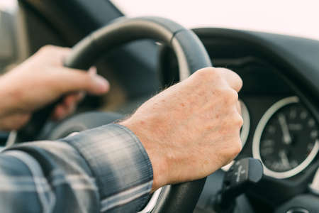 Man's hands holding the steering wheel, driving a car
