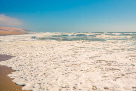 Abstract seascape background. Sandy beach, ocean waves, and clear blue sky on backgroundの写真素材