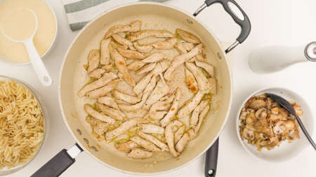 Chopped chicken meat close up on frying pan directly from above. Pasta with chicken, mushrooms, and Alfredo sauce recipeの写真素材