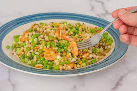 Blend of couscous, orzo, garbanzo beans, red quinoa cooked with shrimps and served with green peas and green onion close up on a plate on white backgroundの写真素材