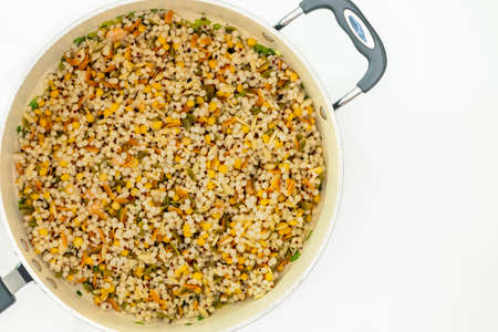 A savory blend of pearled couscous, orzo, baby garbanzo beans, and red quinoa close up on frying pan on white background, flat lay with copy spaceの写真素材