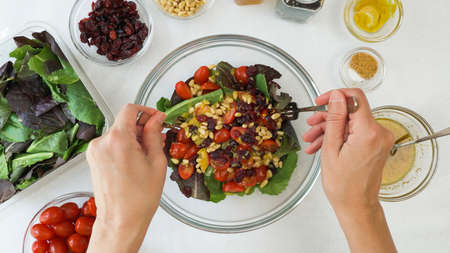 Mixing fresh lettuce salad in a glass bowl. Lettuce salad with cherry tomatoes, dry cranberries, nuts and honey mustard salad dressing recipeの写真素材