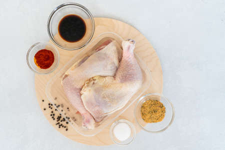 Chicken leg quarters in plastic container and ingredients for marinade, such as paprika, seasoning, salt, soy sauce and spices, close up directly from aboveの写真素材