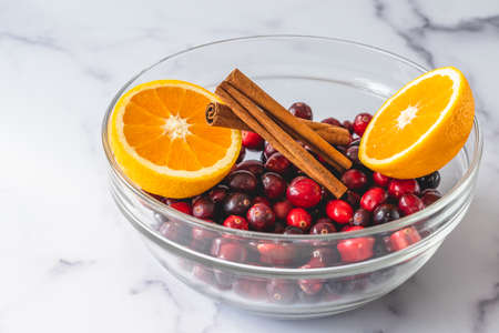 Fresh cranberries, cinnamon and oranges close up in a glass bowl on marble background. Ingredients for cooking cranberry sauceの写真素材