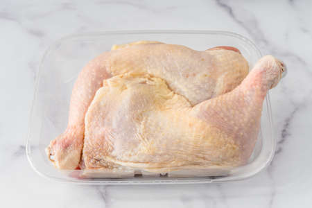 Chicken leg quarters in plastic container close up on marble backgroundの写真素材