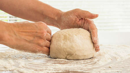 Bread dough or pizza dough close up on wooden kitchen table. Woman hands kneading whole wheat flour...
