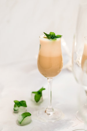 Glass of Irish cream liquor with ice and mint leaves closeup on light grey background