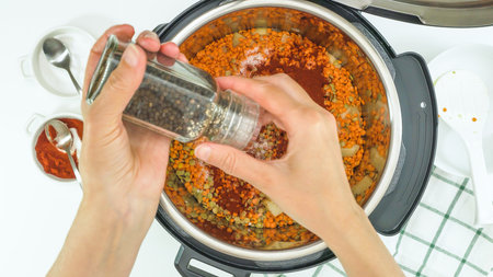 Lentil soup recipe, cooking using modern multi cooker. Woman adds black pepper into potの写真素材