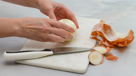 Peeling white onion on marble cutting board. Close up cooking process, woman hands, marble kitchen...