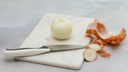 Peeled white onion and knife close up on marble cutting board on kitchen table. Close up cooking process, still lifeの写真素材