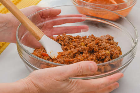 Mix of fried ground beef, fried onion and marinara sauce in a glass bowl close up in woman hands.
