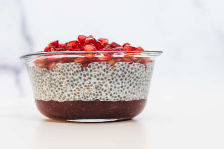 Chia seed pudding with raspberry jam and pomegranate seeds in glass bowl close up on white backgroundの写真素材