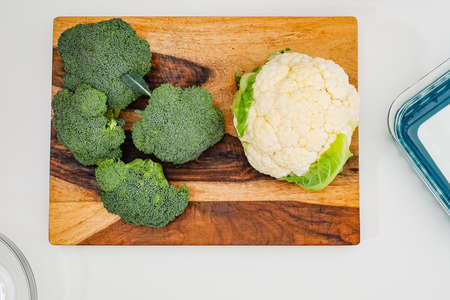 Cauliflower and broccoli close up on wooden cutting board directly from above on light grey...