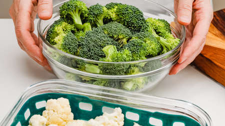 Bowl of fresh raw vegetables, cauliflower and broccoli, close up on kitchen table, woman handsの写真素材