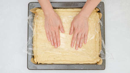Woman's hands placing pizza dough onto baking pan, close up view from above.