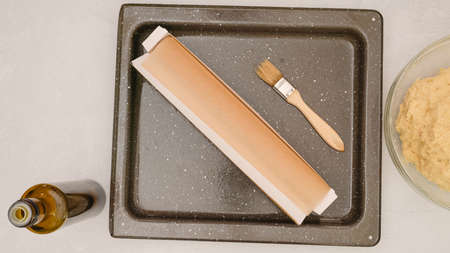 Baking pan, parchment paper, olive oil, and pizza dough in a bowl. Ingredients for baking needs...