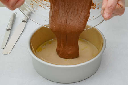 Cake pan lined with parchment paper close up on kitchen table, pouring cake batter into the pan....